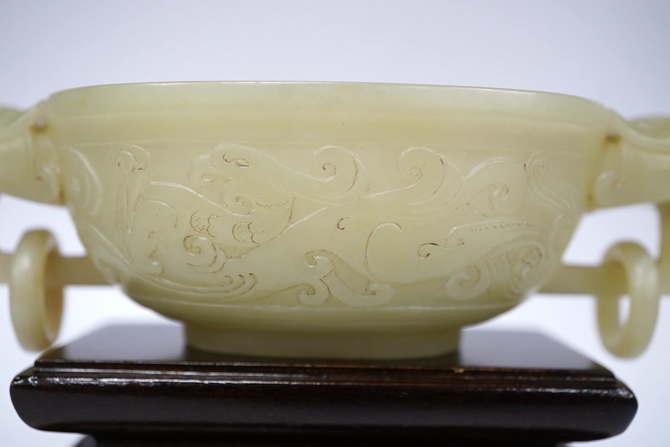 A Chinese archaistic pale green bowenite jade twin handled cup on stand, cup 11.5cm wide. Condition - cup good, stand good